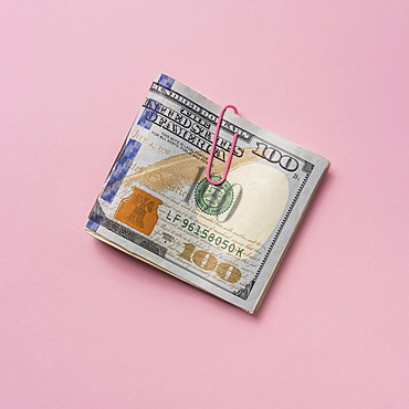 Folded one hundred dollar bill with paper clip on pink background.