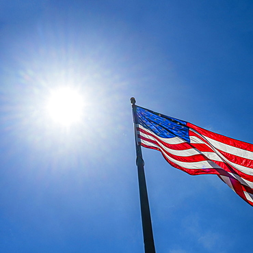 Low angle view of American flag waving in wind against clear sky with Sun