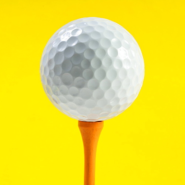 Golf ball on tee against yellow background