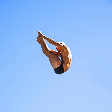 Athletic swimmer mid-air against blue sky