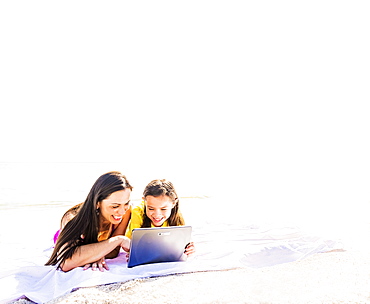 Girl (6-7) lying on beach with her mom and using tablet pc, Jupiter, Florida