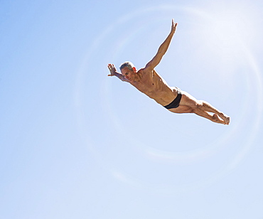 Athletic swimmer mid-air against blue sky