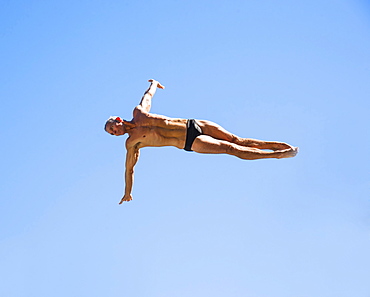 Athletic swimmer mid-air against blue sky