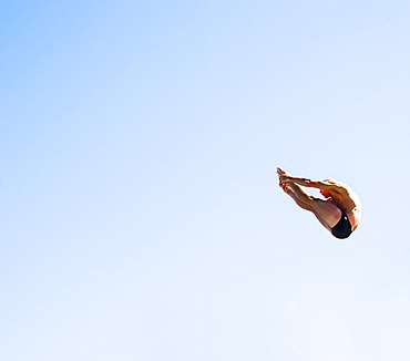 Athletic swimmer mid-air against blue sky