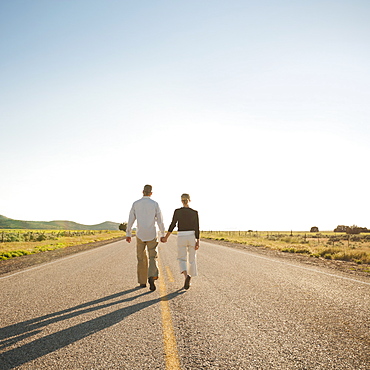 Mid adult couple walking along empty road 