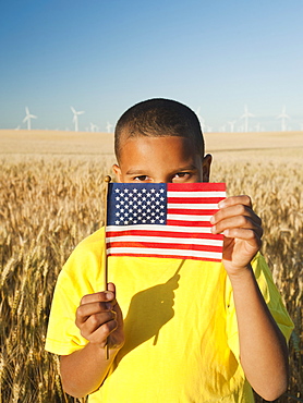 Boy (8-9) holding a small American flag in wheat field