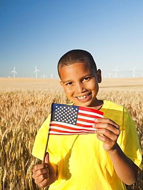 Boy (8-9) holding a small American flag in wheat field