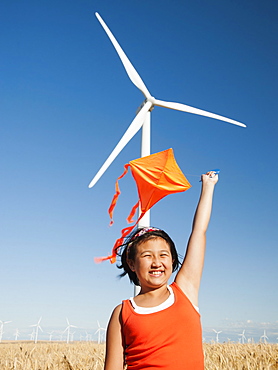 USA, Oregon, Wasco, Girls 10-11) playing with kite in wheat field, wind turbine in background