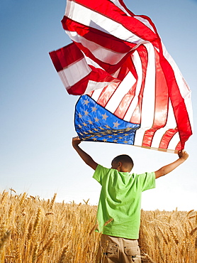 USA, Oregon, Wasco, Boy (8-9) flying american flag in wheat field with wind turbines in background