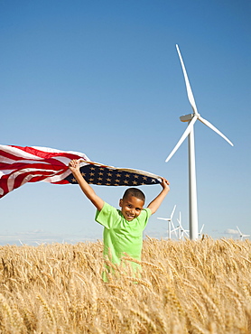 USA, Oregon, Wasco, Boy (8-9) flying american flag in wheat field with wind turbines in background