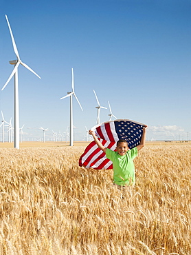 USA, Oregon, Wasco, Boy (8-9) flying american flag in wheat field with wind turbines in background