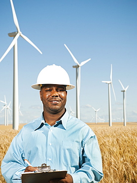 USA, Oregon, Wasco, Engineer standing in wheat field in front of wind turbines