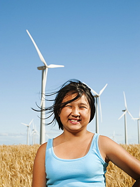 USA, Oregon, Wasco, Cheerful girl (10-11) standing in wheat field with wind turbines in background