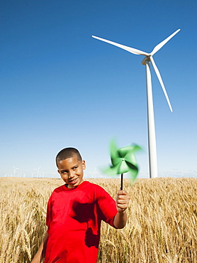 USA, Oregon, Wasco, Girl (10-11) holding fan in wheat field with wind turbines in background