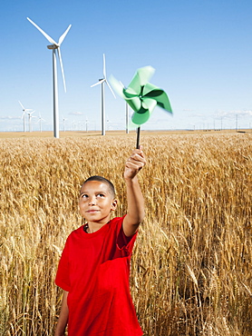 USA, Oregon, Wasco, Girl (10-11) holding fan in wheat field with wind turbines in background