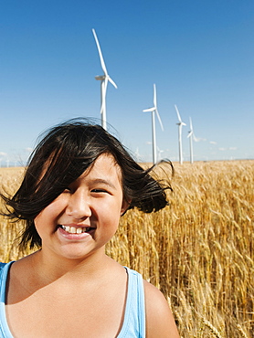 USA, Oregon, Wasco, Cheerful girl (10-11) standing in wheat field with wind turbines in background