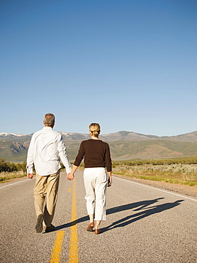 Mid adult couple walking along empty road 