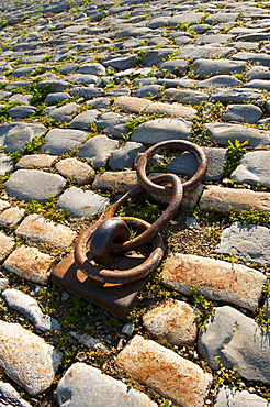 Rusty chain anchored to the ground amongst cobblestones