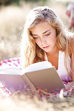 Teenage girl (16-17) reading book outdoors