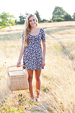 Happy teenage girl (16-17) standing in meadow, holding picnic basket