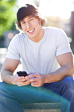 Young man sitting outdoors, text messaging