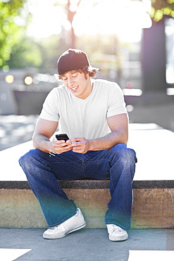 Young man sitting outdoors, text messaging