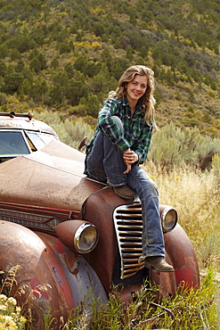 USA, Colorado, Portrait of woman resting on abandoned truck in desert