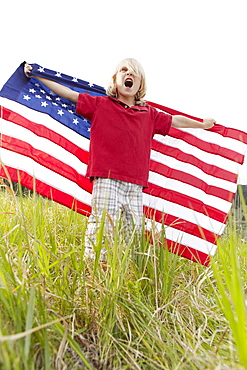 Boy (6-7) waving American flag in meadow