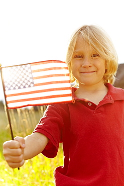 Portrait of boy (6-7) waving American flag in meadow