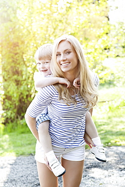 Young woman giving piggyback ride to son (2-3) in park