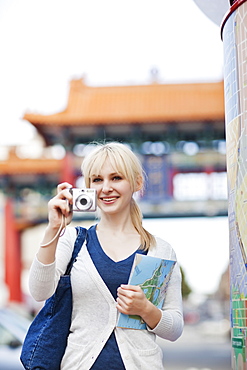 USA, Seattle, Young woman taking photos and holding map