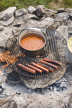 Grilled sausages and beans on campfire