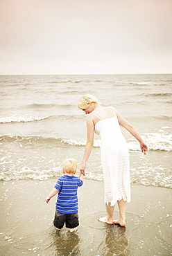 Mother and child walking hand in hand at the water's edge