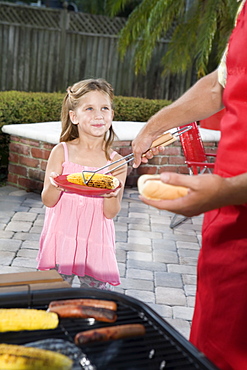 Father at barbecue grill serving daughter hot dog