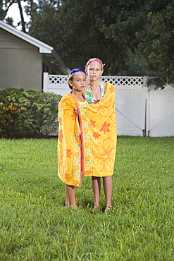 Portrait of sisters wrapped in towel standing in backyard