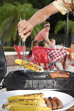 Man grilling hotdogs and corn in backyard