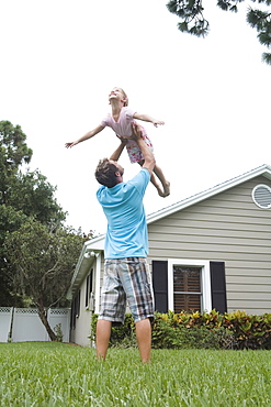 Father lifting daughter in backyard