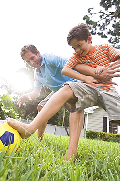 Father and son playing soccer in backyard