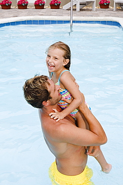 Father lifting daughter out of swimming pool