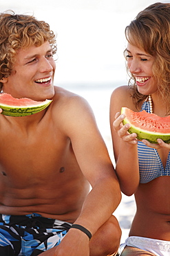 Young couple eating watermelon on beach