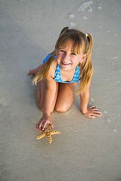 Girl picking up starfish, Florida, United States