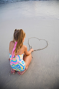 Girl drawing heart in sand, Florida, United States