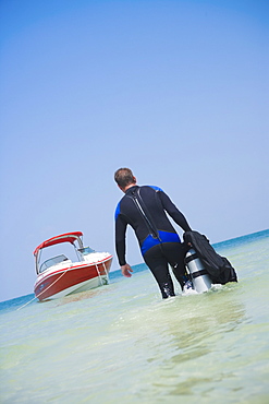 Man carrying scuba gear towards boat, Florida, United States