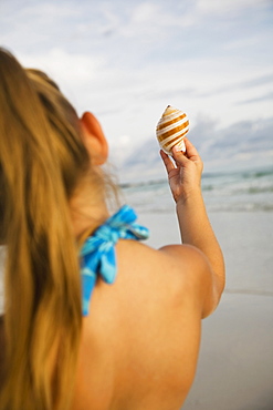 Girl holding up sea shell, Florida, United States