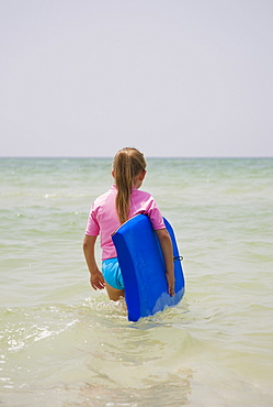 Young girl walking into water with boogie board, Florida, United States