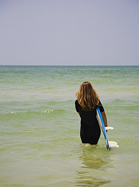 Girl walking into water with surfboard, Florida, United States