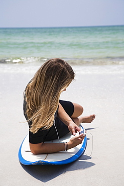 Girl listening to mp3 player on surfboard, Florida, United States