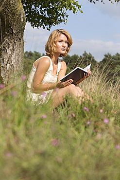 Woman sitting on grass and reading book, Netherlands, Gelderland, Hatertse Vennen