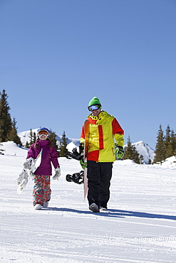 USA, Colorado, Telluride, Father and daughter (10-11) walking with snowboards in winter scenery