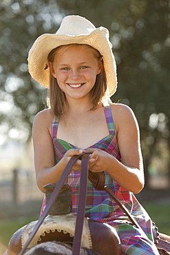 Portrait of smiling cowgirl (8-9) horseback riding in ranch